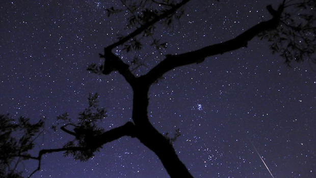 In this photo taken with long shutter speed, a meteor sparks, lower right, while entering the earth's atmosphere behind an olive tree during the Perseids Meteor Shower, in Fanos village, central Greece, on Saturday, Aug. 10, 2013.