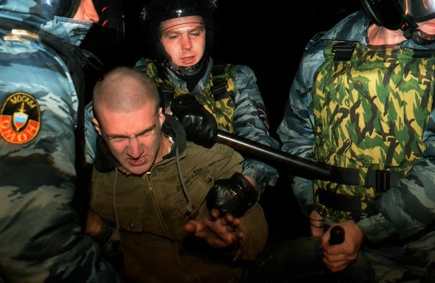 Russian riot police escort a man detained during mass rioting in the southern Biryulyovo district of Moscow