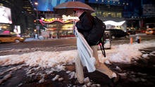 A businessman carries an umbrella and a dress shirt on a hanger while making his way through slush and snow in New York's Times Square Feb. 5, 2014.