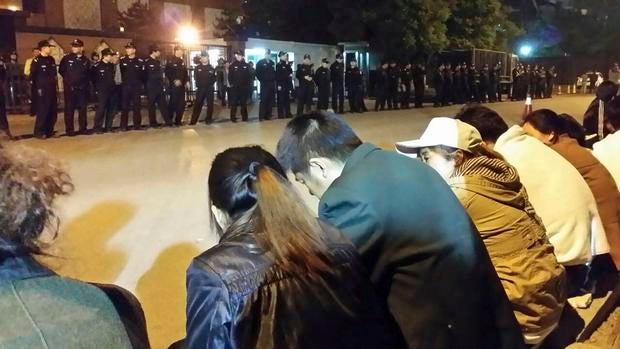 Family members (front) of passengers aboard missing Malaysia Airlines flight MH370 gather for a sit-in protest as security personnel stand guard outside the Malaysian Embassy in Beijing