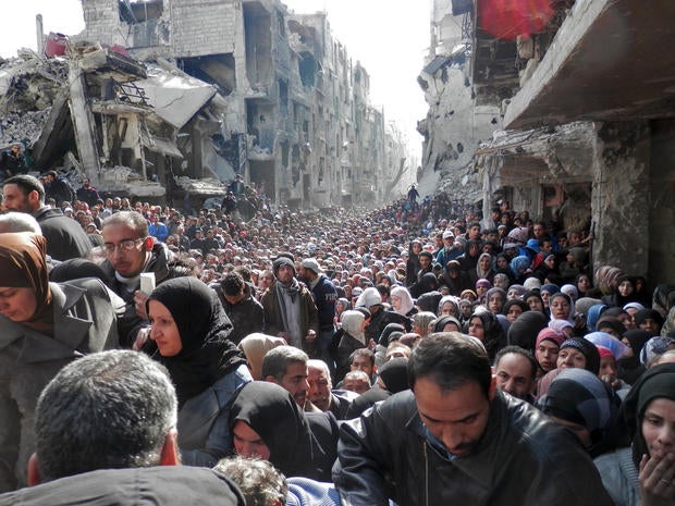 Residents wait in line to receive food aid distributed in the Yarmouk refugee camp in Damascus