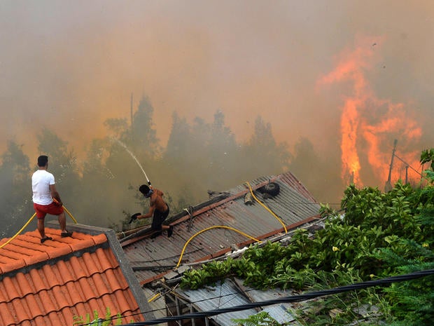 Men spray water on the roofs of houses to protect them from an approaching fire in Portugal's Maderia islands