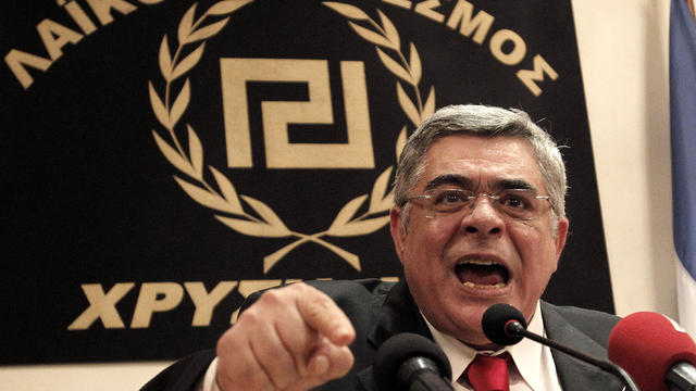 Golden Dawn leader Nikolaos Michaloliakos speaks during a news conference in front of a banner with the twisting Maeander, an ancient Greek decorative motif that the party has adopted as its symbol, in Athens, Greece, May 6, 2012. 