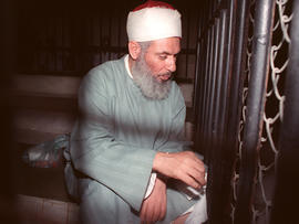 Blind sheik Omar Abdel-Rahman sits and prays inside an iron cage at the opening of court session in Cairo Aug 6 1989