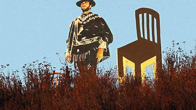 Life-sized cardboard cutout of actor Clint Eastwood next to two empty chairs -- one wooden, in left background, and one cardboard, is seen overlooking freeway in Glendale, Calif. 
