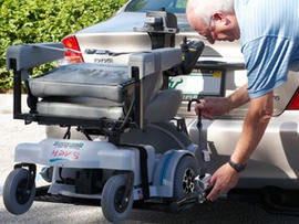 An older gentleman fiddles with a Hoveround wheelchair lift.