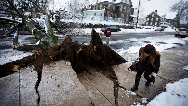 A woman ducks under a utility line next to an ice-covered downed tree that landed atop a minivan after a winter storm Feb. 5, 2014, in Philadelphia.