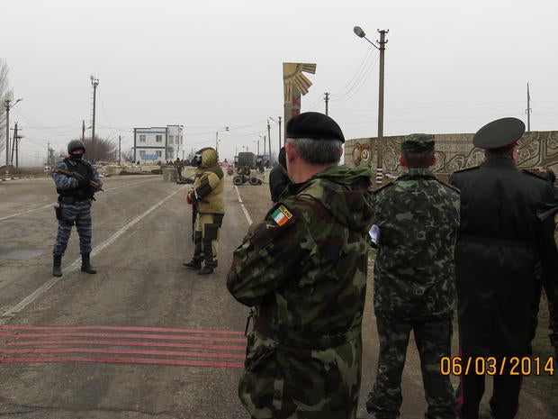 Members of an Organisation for Security and Cooperation in Europe (OSCE) military observer mission (at right, facing away from camera) are stopped at the Crimean border by unknonw armed men
