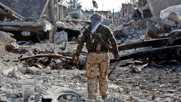 A Kurdish People's Protection Unit (YPG) fighter shows the extent of the damage from a truck bomb in Kobani, Syria, Nov. 19, 2014.