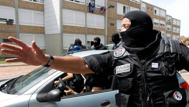 A French special police forces officer gestures as police escort a woman from a residential building during a raid in Saint-Priest, near Lyon, France, June 26, 2015.