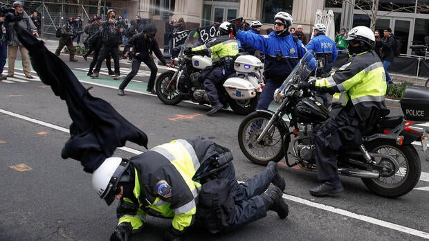 A police officer falls to the ground as another shoots pepper spray at protesters demonstrating against President Trump on the sidelines of the inauguration in Washington Jan. 20, 2017.