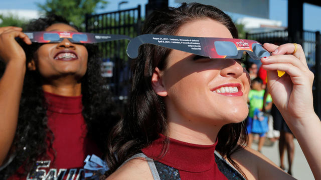 Cheerleaders use solar viewing glasses before welcoming guests to the football stadium to watch the total solar eclipse at Southern Illinois University in Carbondale 