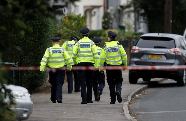 Police officers walk behind cordon tape set up around a property being searched after a man was arrested in connection with an explosion on a London Underground train, in Sunbury-on-Thames
