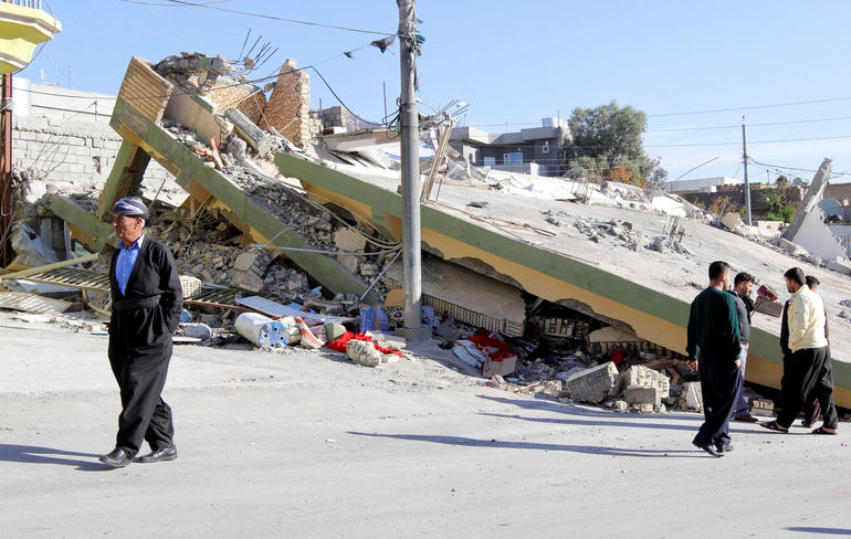 People walk past a damaged building following an earthquake in the town of Darbandikhan 