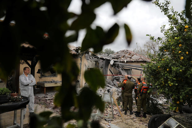 An Israeli police sapper and soldiers work next to a house that was hit by a rocket north of Tel Aviv, Israel 