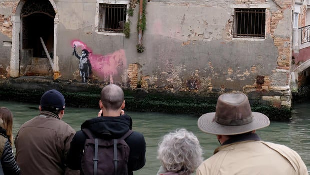 People look at the new work of British street artist Banksy, on the outer wall of a house along the Rio de Ca Foscari canal in Venice