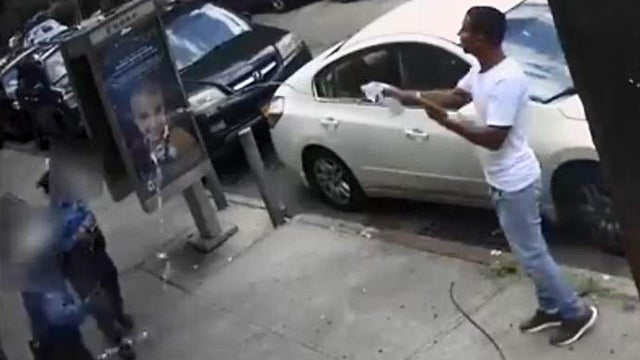 A man throws water at two New York Police Department traffic enforcement agents in the Queens borough of New York City July 24, 2019, in an image capture of surveillance video released by the NYPD Crime Stoppers Program. 