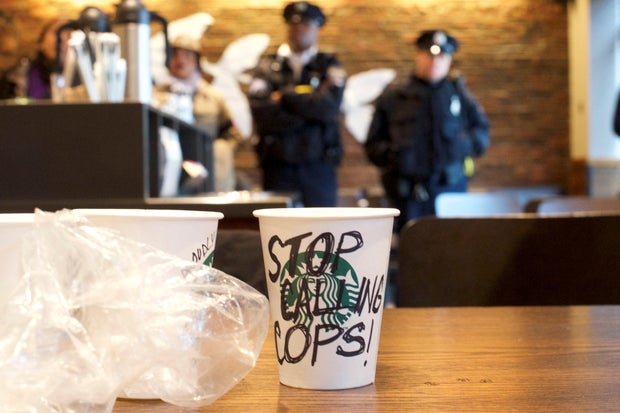 A Starbucks coffee cup with "Stop Calling Cops!" written on the side sits on a table as police monitor protestors demonstrating inside a Center City Starbucks, where two black men were arrested, in Philadelphia