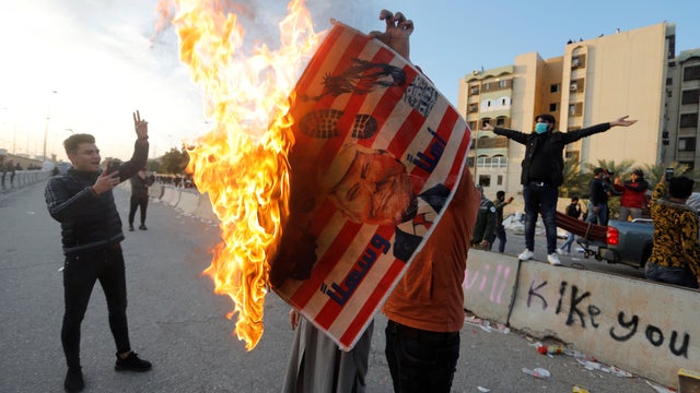 A protester holds a placard with an illustration of President Trump burning outside the U.S. Embassy in Baghdad, Iraq, January 1, 2020, during a protest to condemn airstrikes against an Iran-backed militia. 