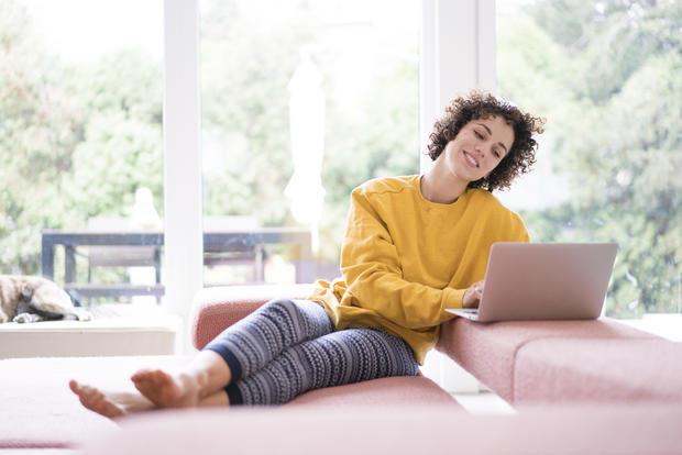 Smiling woman using laptop on couch at home 
