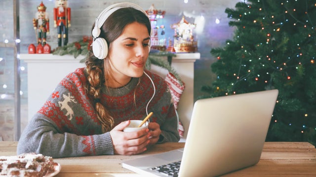 Woman with cup of coffee using laptop and headphones at Christmas time 
