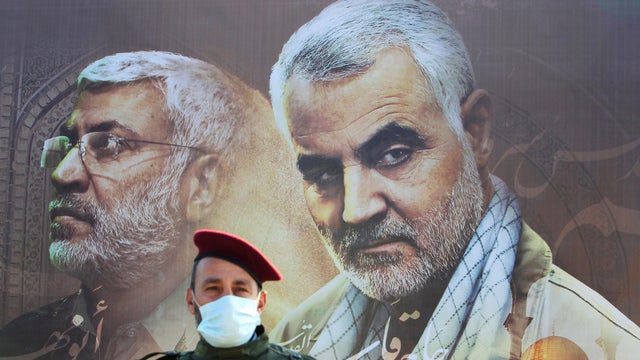 A member of Lebanon's Hezbollah stands in front of a picture depicting senior Iranian military commander General Qassem Soleimani and Iraqi militia commander Abu Mahdi al-Muhandis, during a ceremony marking the first anniversary of their killing, in Khiam 