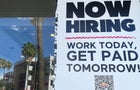 Sign reading "Now hiring. Work today, get paid tomorrow!" with palm tree reflection in the background 