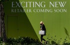 Woman walks by full-frame green sign reading "Exciting new retailer coming soon" 
