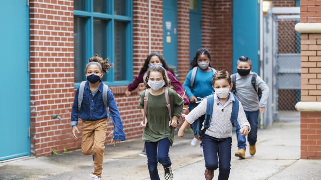 School children with face masks running outside building 
