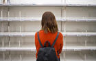 Young woman standing in front of empty shelf in a supermarket 