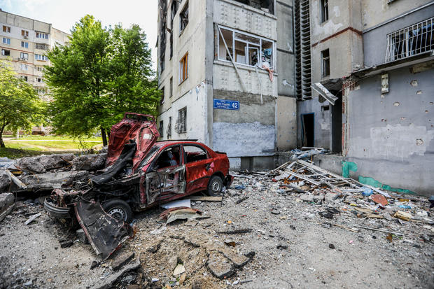 A destroyed car in front of a residential building following 